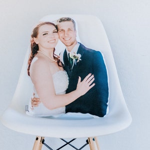 May include: A white cushion featuring a printed photograph of a bride and groom. The bride is wearing a white strapless gown and the groom is wearing a black suit. They are both smiling and looking at the camera.