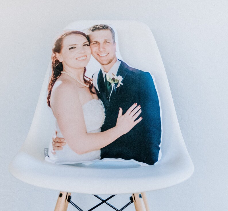 May include: A white cushion featuring a printed photograph of a bride and groom. The bride is wearing a white strapless gown and the groom is wearing a black suit. They are both smiling and looking at the camera.