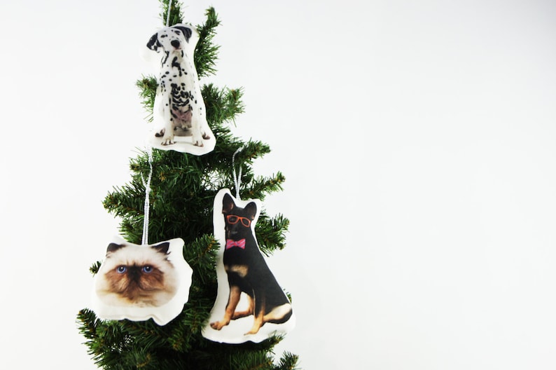 Peut inclure: Un sapin de No&euml;l d&eacute;cor&eacute; de trois ornements sur le th&egrave;me des animaux de compagnie. Les ornements repr&eacute;sentent un dalmatien, un chat Ragdoll et un berger allemand portant des lunettes et un n&oelig;ud papillon. Chaque ornement est blanc avec une image d'animal.