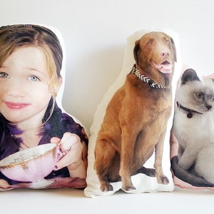 May include: Three personalised pillows featuring images of a girl, a brown dog, and a white cat. The pillows are white with a light pink border.