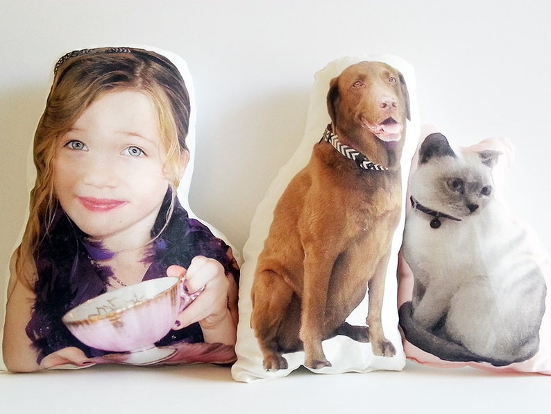 May include: Three personalised pillows featuring images of a girl, a brown dog, and a white cat. The pillows are white with a light pink border.