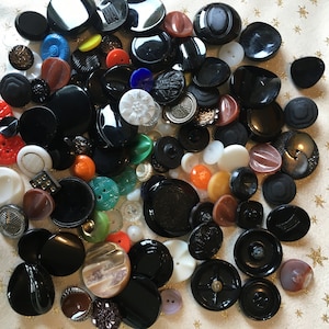 May include: A large collection of vintage buttons in various colors and styles, including black, white, red, orange, and green. The buttons are made of different materials, such as plastic, metal, and glass.