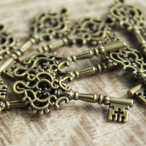 Peut inclure: Une collection de petites clés en métal de style ancien dans un ton bronze. Chaque clé présente un design complexe en filigrane ajouré sur l'anneau, une tige cylindrique fine et un panneton rectangulaire avec un motif cranté distinct.