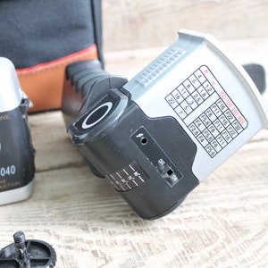 May include: A black and silver camera with a motor drive and red eye reduction. The camera has a flash unit attached to it. The flash unit has a chart with ISO and aperture settings.