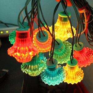 Könnte beinhalten: Eine Lichterkette mit bunten Lichtern in verschiedenen Farben, darunter Rot, Grün, Blau und Gelb. Die Lichter sind in Form kleiner, runder Laternen.