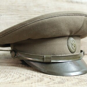 May include: A green military-style cap with a black leather band and a metal badge featuring a star and a hammer and sickle.