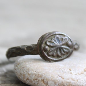 May include: Antique silver ring with an oval face featuring a floral design. The band has a hammered texture, and the ring shows signs of age and wear, suggesting it is vintage or an antique piece.