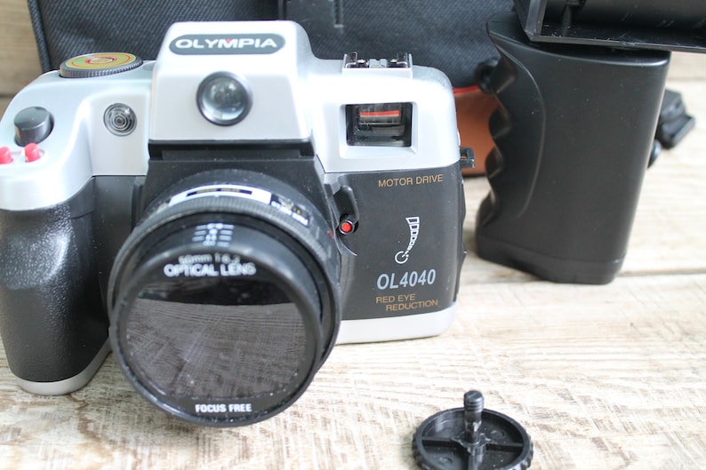 May include: A silver and black 35mm film camera with a black lens and the text "OLYMPIA OL4040 MOTOR DRIVE RED EYE REDUCTION" on the side.