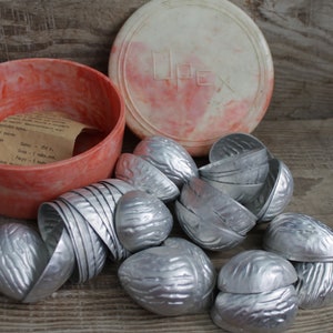May include: A set of 18 silver-colored metal molds shaped like walnut halves, in a red and white plastic container with the word "Upex" printed on the lid.