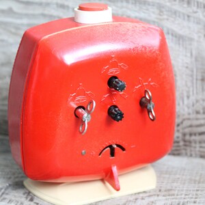 May include: A red wind-up alarm clock with three keys on the front. The clock has a white base and a red button on top.