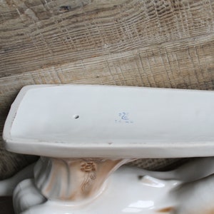 May include: White porcelain figurine of a woman holding a tray. The tray has a blue mark on the bottom that reads "22C".