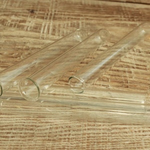 Puede incluir: Cuatro tubos de ensayo de vidrio transparente de diferentes longitudes están dispuestos sobre una superficie de madera.