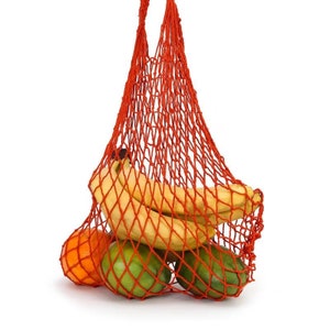 Puede incluir: Una bolsa de red roja llena de fruta fresca. La bolsa contiene plátanos, naranjas y fruta verde. La bolsa está suspendida sobre un fondo blanco, mostrando los colores vibrantes de los productos.
