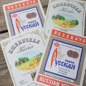 Puede incluir: Tres etiquetas de vodka rusa vintage con el texto "Pshemichnaya Vodka" y "Russkaya Vodka" en escritura cirílica. Las etiquetas están impresas en papel blanco con acentos rojos, azules y dorados. Las etiquetas presentan ilustraciones de campos de trigo y una imagen estilizada de una hoz.