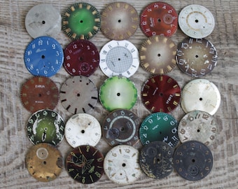 May include: A collection of 25 vintage watch faces in various colors and styles. The faces are round and have different numbers, markings, and designs. Some of the faces are worn and have a patina.