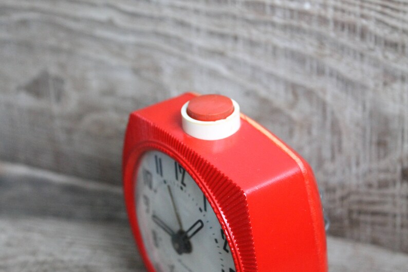 May include: A red alarm clock with a white face and black hands. The clock has a red button on the top.