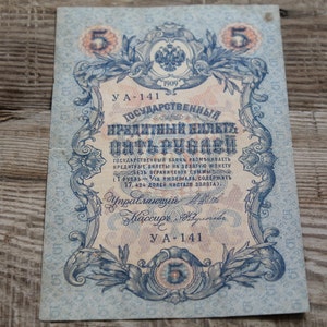 May include: A vintage Russian five ruble banknote from 1909. The note features an ornate design with a central image of the Russian Imperial Eagle and the text "Государственный кредитный билет Пять рублей" (State Credit Note Five Rubles).