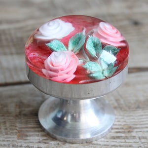May include: A silver cabinet knob with a clear dome containing pink and white roses and green leaves.