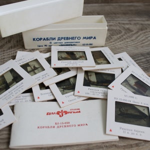 Puede incluir: Una colección de diapositivas antiguas con imágenes de barcos antiguos, con texto en ruso. Las diapositivas están en marcos blancos y están esparcidas alrededor de una caja blanca y un folleto. La caja y el folleto también tienen texto.