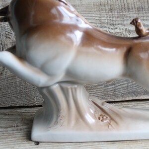 May include: A white and brown ceramic bull figurine with a small bird perched on its tail. The bull is standing on a base with a textured surface.