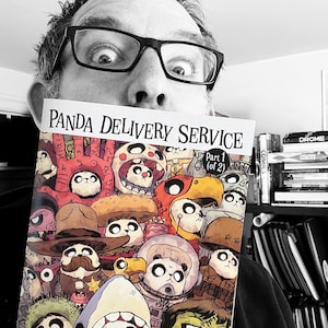 May include: A comic book titled "Panda Delivery Service" Part 1 (of 2) is held up in front of a person's face. The cover art features numerous panda characters in various costumes and hats. The background is a bookshelf with other books.