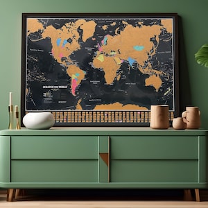 May include: A framed world map with a black background and gold foil detailing. The map is labeled "SCRATCH THE WORLD". The map is displayed on a green cabinet with wooden accents and decorative items.