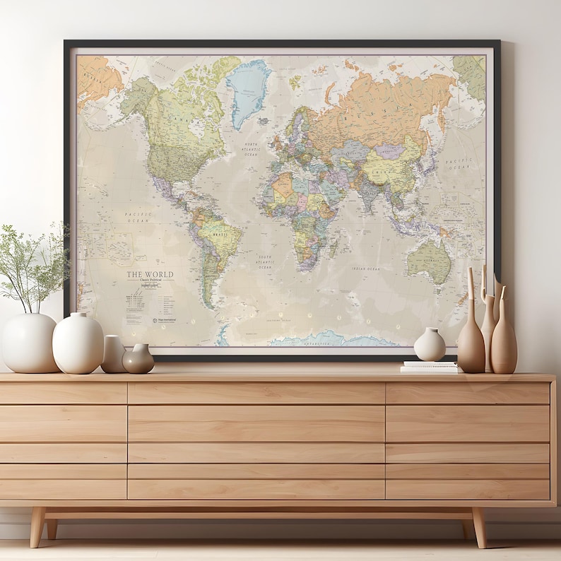May include: A framed world map with a beige background and colorful country borders. The map is titled "The World" and includes a legend with various symbols and abbreviations. The map is hanging on a wall above a wooden dresser.