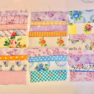 May include: A collection of fabric strips in various floral patterns, including pink, yellow, blue, and white. The strips are arranged in rows, creating a patchwork effect.