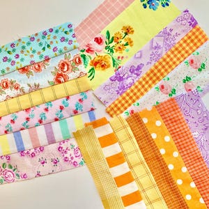 May include: Assortment of colourful fabric scraps in various patterns, including floral, striped and checkered designs. The fabrics are arranged in a layered, overlapping pattern, creating a visually appealing and textured display.