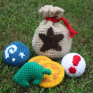 Puede incluir: Juguetes de peluche tejidos a crochet inspirados en la serie de videojuegos Animal Crossing. El conjunto incluye una bolsa de dinero marrón con una estrella, una bola azul con una luna creciente blanca y una estrella, una hoja verde, una moneda amarilla y naranja, y una bola blanca con un signo de exclamación rojo.