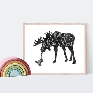 May include: Black and white illustration of a moose kissing a goose with the text "Have you ever seen a moose kissing a goose" printed on the moose's body. The illustration is framed in a light wood frame.