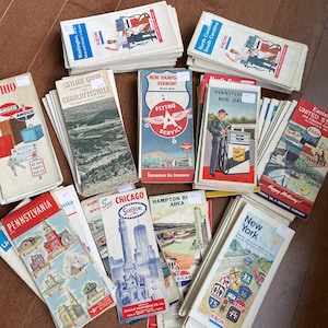 May include: A collection of vintage travel maps and brochures, featuring various states and regions. The maps showcase colorful illustrations and text, including "New York," "Chicago," and "Pennsylvania." The maps are from various oil companies.