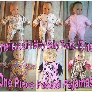 May include: Six American Girl Bitty Baby Twins dolls wearing one-piece footed pajamas. The pajamas are in various patterns, including floral, animal, and polka dots. The dolls are approximately 15 inches tall.
