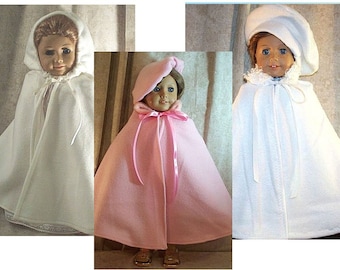 May include: Three doll outfits: a white hooded cape with a lace trim, a pink hooded cape with a matching hat, and a white cape with a beret-style hat. Each cape has a ribbon tie closure. The dolls are wearing the capes.