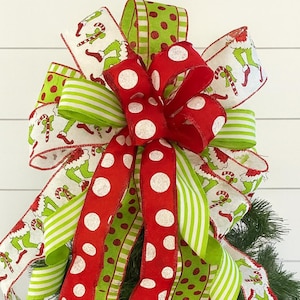 May include: A festive Christmas bow featuring red and white polka dot ribbon, green and white striped ribbon, and ribbon with a cartoon character design. The bow is a vibrant mix of colors, perfect for holiday decor.