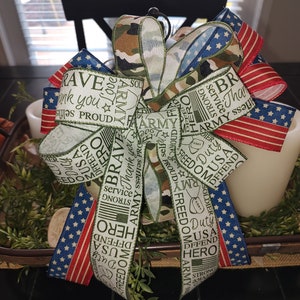 May include: A green, white, and camouflage ribbon bow with red, white, and blue stars and stripes ribbon. The ribbon has the words "Army", "Hero", "Brave", "Duty", "Freedom", "USA", "Strong", "Service", "Thank you", "Proud", "Defend", "Soldier", and "I Less" printed on it.