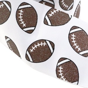 May include: White ribbon with a repeating pattern of brown footballs. Each football has white laces and end stripes. The ribbon is likely used for crafting, gift wrapping, or sports-themed decorations.