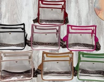 May include: Eight clear plastic crossbody bags with different colored trim. The bags have a clear front pocket and a smaller clear back pocket. The bags have a leopard print strap.