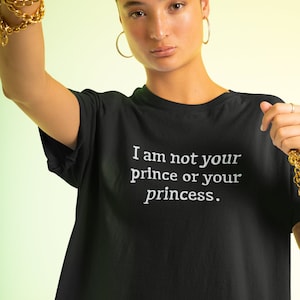 Może przedstawiać: Osoba w czarnym t-shircie z nadrukiem "I am not your prince or your princess." w kolorze białym.