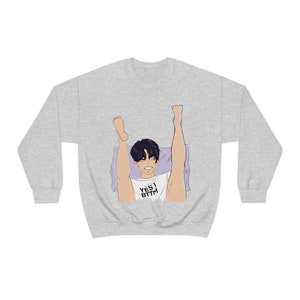 Könnte beinhalten: Ein graues Sweatshirt mit einem grafischen Aufdruck einer Person, die auf einem Kissen liegt und die Beine in die Luft streckt. Der Text "YES I BTTM" ist auf dem Shirt aufgedruckt.