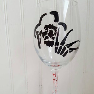 Pu&ograve; includere: Un bicchiere da vino in vetro trasparente con una silhouette nera di un personaggio di un film horror sul davanti. Il bicchiere ha schizzi di vernice rossa sul gambo e sulla base.