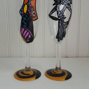 Pode incluir: Duas ta&ccedil;as de champanhe pintadas &agrave; m&atilde;o com desenhos de espiral preto e dourado na base. Uma ta&ccedil;a apresenta uma imagem pintada &agrave; m&atilde;o de Jack Skellington de O Estranho Mundo de Jack. A outra ta&ccedil;a apresenta uma imagem pintada &agrave; m&atilde;o de Sally de O Estranho Mundo de Jack.