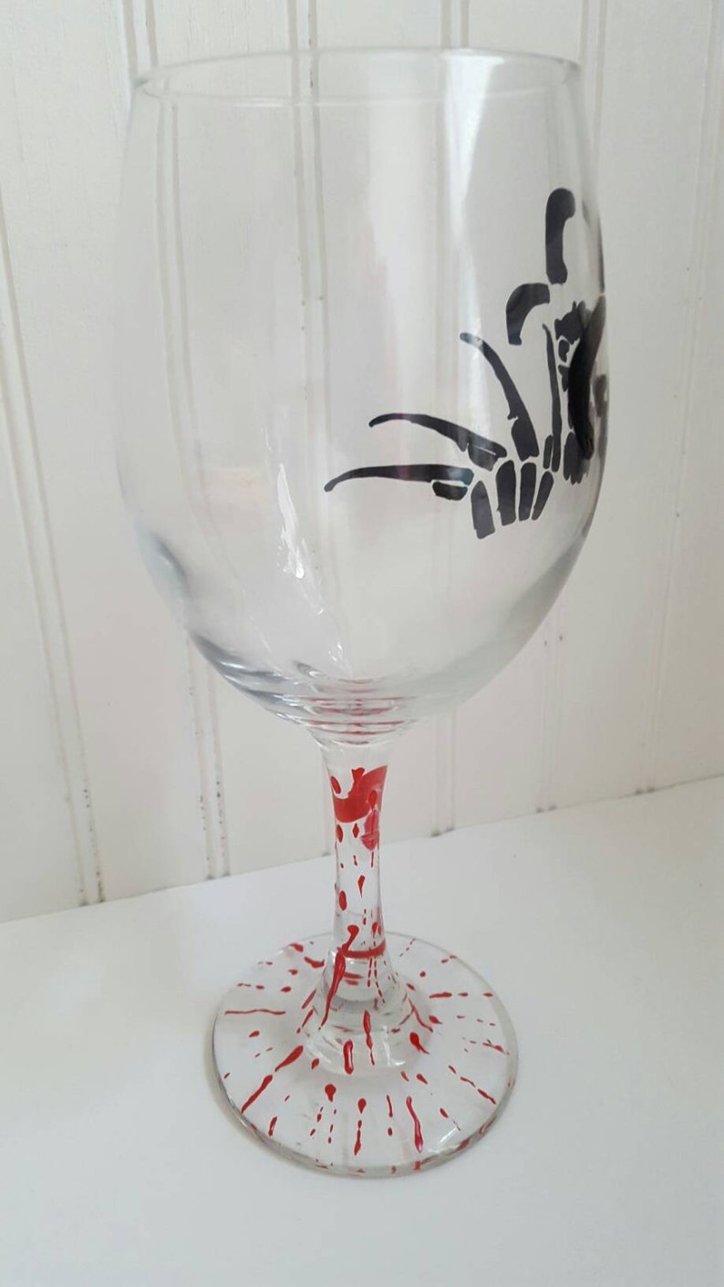 Pu&ograve; includere: Un bicchiere di vino in vetro trasparente con una silhouette nera di una mano con artigli sul lato. La base del bicchiere &egrave; dipinta con vernice rossa a spruzzo.