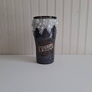 May include: A black and silver glitter tumbler with a white pearl rim and a label that reads "Toe of Frog, Crazy Elf Potion Supplier".