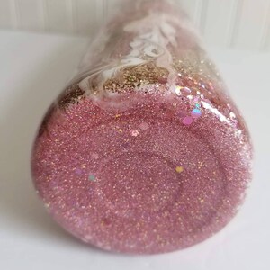 May include: A pink glitter tumbler with white and gold swirls. The tumbler is filled with pink glitter and has a clear lid.