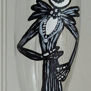 Pode incluir: Uma ta&ccedil;a de vinho de vidro transparente com uma ilustra&ccedil;&atilde;o pintada &agrave; m&atilde;o em preto e branco de Jack Skellington do filme O Estranho Mundo de Jack. A ilustra&ccedil;&atilde;o mostra Jack Skellington em p&eacute; com seu sorriso caracter&iacute;stico.