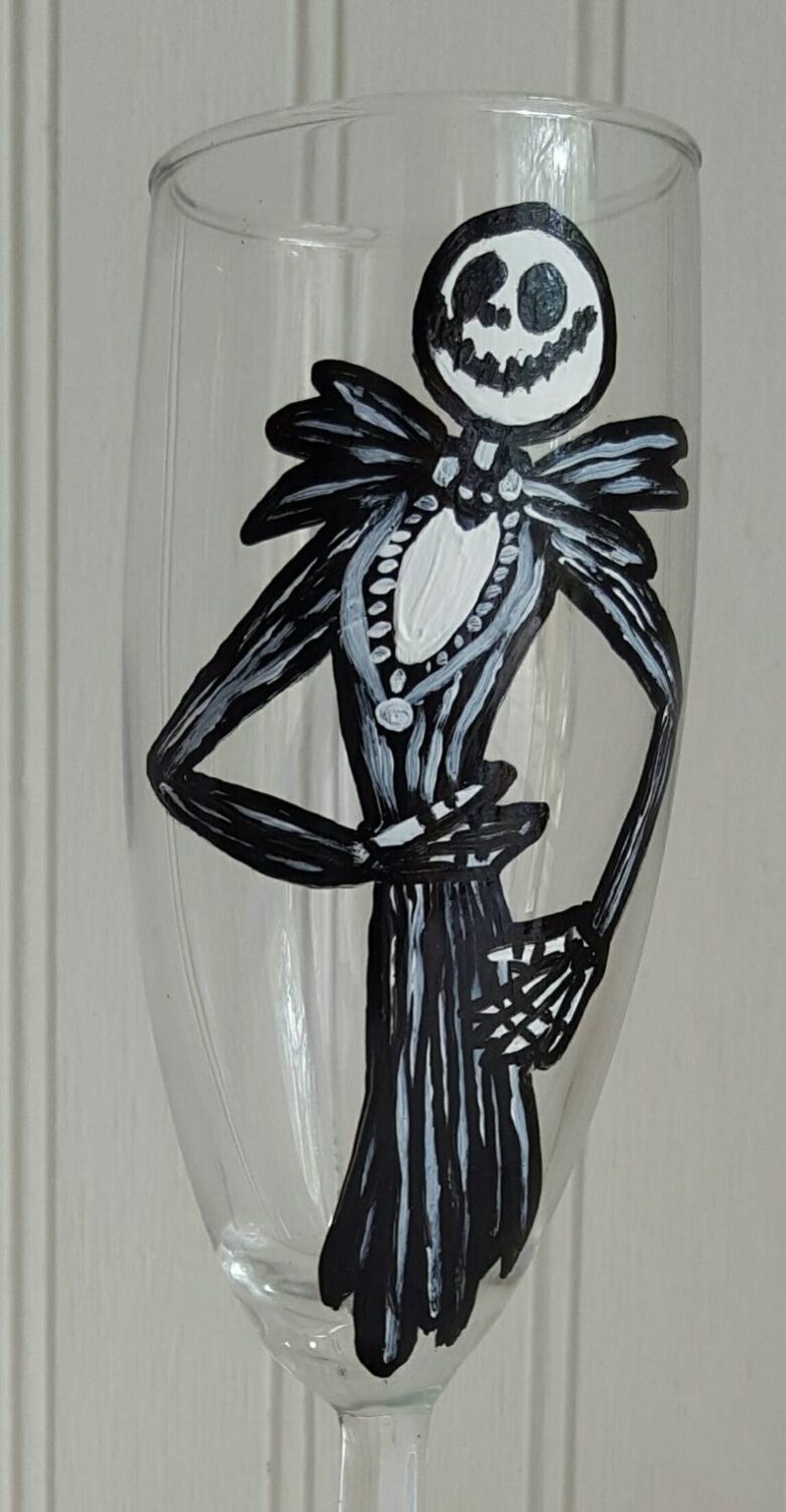 Pode incluir: Uma ta&ccedil;a de vinho de vidro transparente com uma ilustra&ccedil;&atilde;o pintada &agrave; m&atilde;o em preto e branco de Jack Skellington do filme O Estranho Mundo de Jack. A ilustra&ccedil;&atilde;o mostra Jack Skellington em p&eacute; com seu sorriso caracter&iacute;stico.