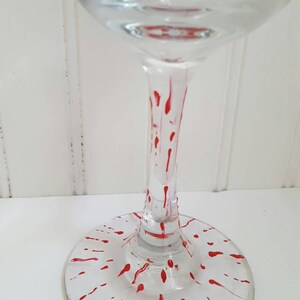 Pu&ograve; includere: Un bicchiere da vino in vetro trasparente con un motivo a spruzzo rosso sulla base e sul gambo.