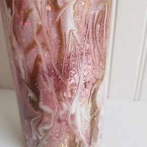 May include: A pink and white tumbler with gold glitter swirls. The tumbler has a marbleized design with a pink, white, and gold color scheme.