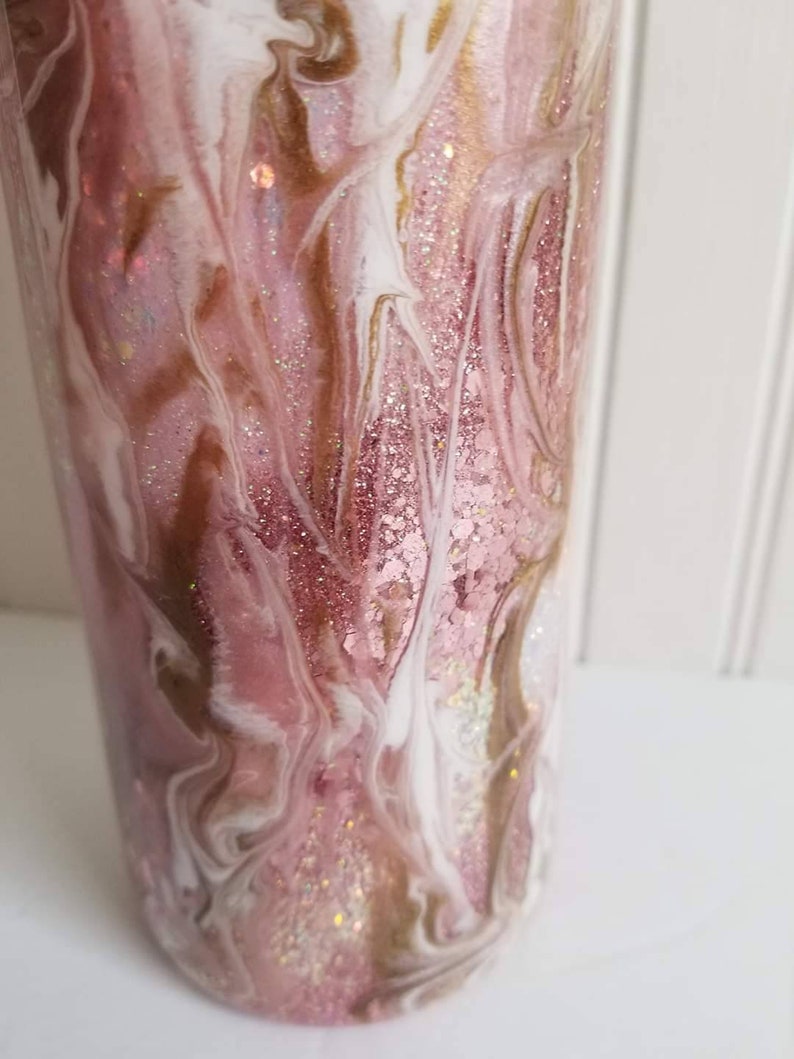 May include: A pink and white tumbler with gold glitter swirls. The tumbler has a marbleized design with a pink, white, and gold color scheme.